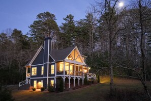 A two-story house with a wrap-around porch, a chimney, and a large window overlooking a forested area. - Elegant Murray Cove at Lake Burton (Tiger)