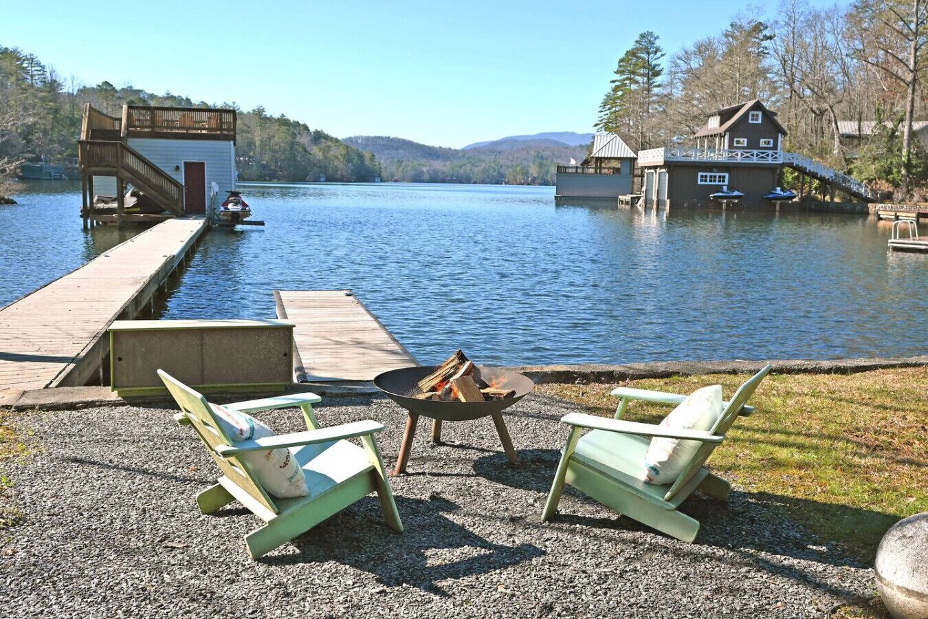 Een landschap bij een meer met een steiger, een vuurkuil en twee Adirondack stoelen.