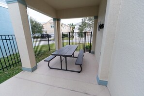 Ein überdachter Patio-Bereich mit Picknicktisch und Bänken, umgeben von einem niedrigen Zaun und einer weißen Mauer.