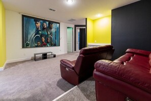 Ein Heimkino-Raum mit einem großen Flachbildfernseher, zwei roten Ledersesseln und einem Teppichboden.