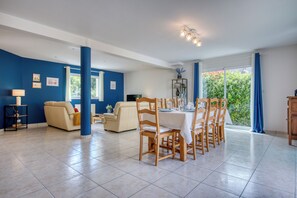 A spacious living area with a dining table set for six, a sofa, and a television. - Les Azurs d'Erdeven - Terrasse - Plage (Erdeven)