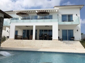 Ein modernes, zweistöckiges Haus mit Swimmingpool, überdachter Terrasse und Balkon.