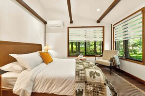 Een hotelkamer met een bed, een stoel, een raam met jaloezieën en uitzicht op groen.