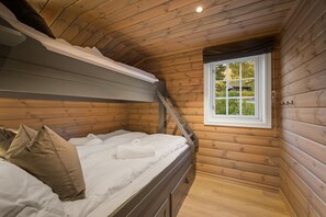 A wooden cabin room with a bunk bed, a window with a view, and a small balcony.