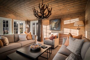 A cozy log cabin interior with a wooden ceiling, a fireplace, a sofa, a chair, and a dining table. - The Nordic Retreat - Stryn (Vestland)