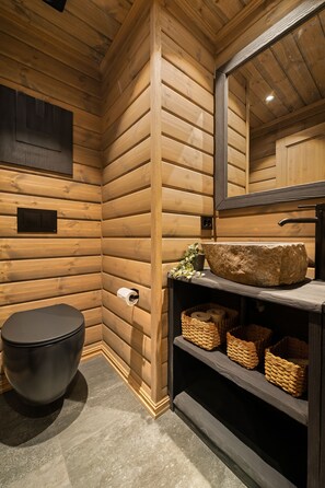 A wooden cabin bathroom with a toilet, a large mirror, and a stone basin.