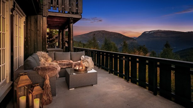 Ein hölzerner Balkon mit einer Couch, einem kleinen Tisch mit Kerzen und Blick auf Berge.