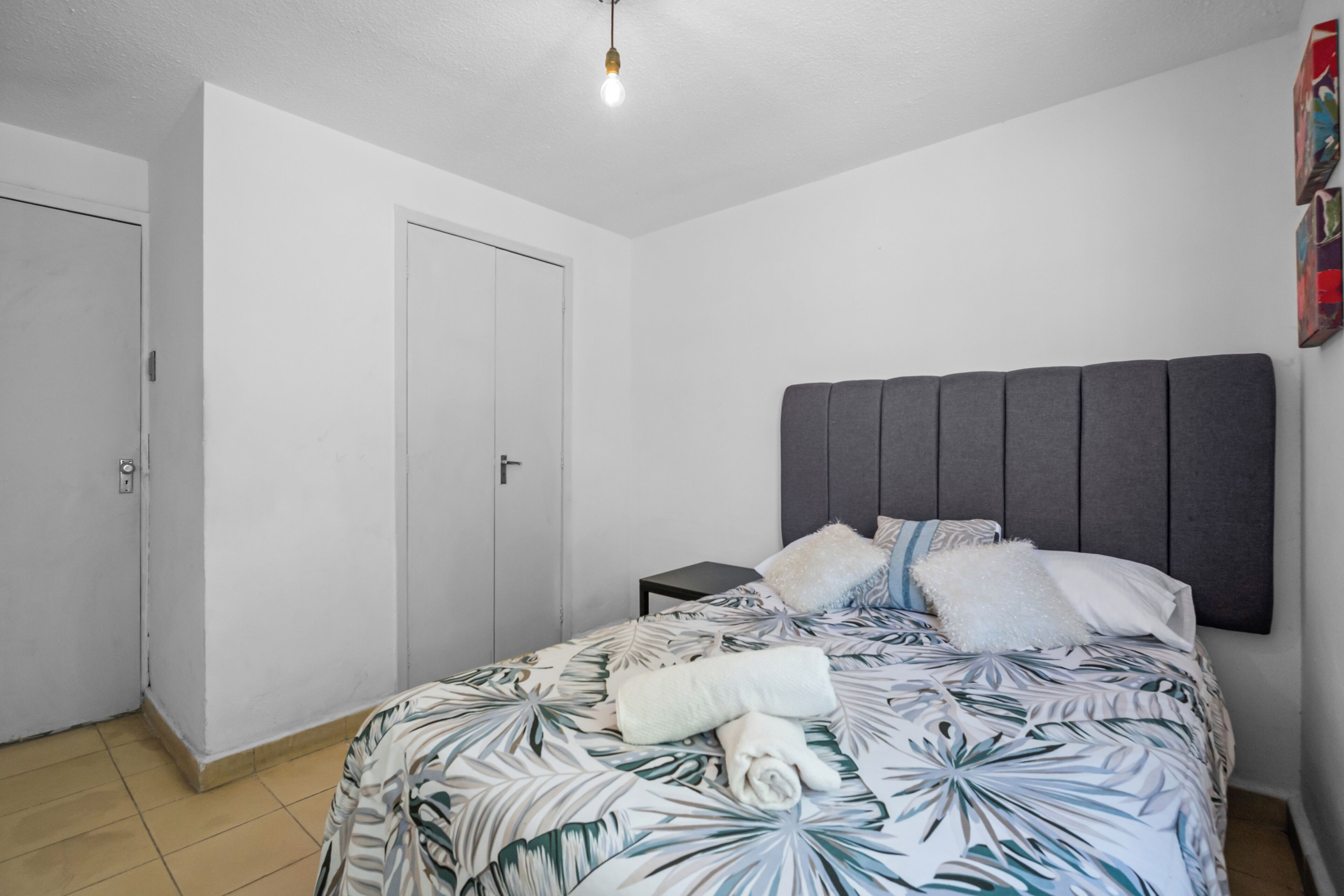 Un dormitorio con una cama, una mesita de noche, una puerta y una lámpara.