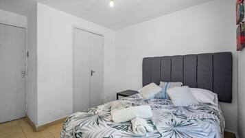 Un dormitorio con una cama, una mesita de noche, una puerta y una lámpara.
