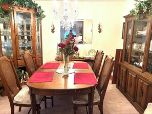 Une salle à manger avec une table en bois, des chaises, un lustre et des vitrines contenant des objets décoratifs.