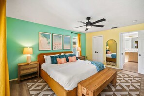 A bedroom with a bed, bedside tables, a ceiling fan, and a bathroom visible through an open door. - Sports Court,  Heated Pool, Mini Golf, Fire Pit, Game Room in Bradenton (Bradenton)