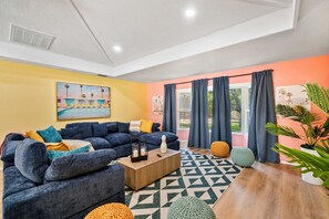 A modern living room with a blue sofa, a wooden coffee table, and a colorful geometric rug. - Sports Court,  Heated Pool, Mini Golf, Fire Pit, Game Room in Bradenton (Bradenton)