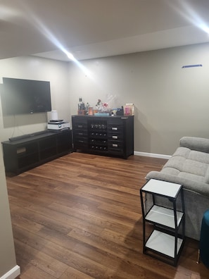A living room with a flat-screen TV, a dark wooden cabinet, a gray sofa, and a small black table. - Cozy 1-bedroom apartment in lovely Saint Georges with AC (Saint Georges)