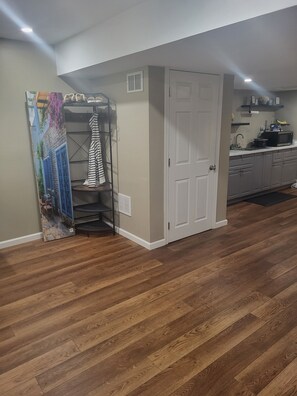Ein Zimmer mit Holzboden, einer weißen Tür, einer Küchenzeile mit Schränken und einem Kleiderständer mit gestreifter Kleidung.