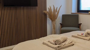 Quarto de hotel com uma cama grande, televisão de tela plana fixada em uma parede revestida de madeira, uma cadeira e uma janela.