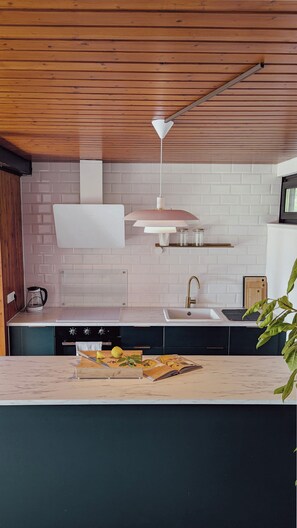 A kitchen with a wooden ceiling, white brick backsplash, a sink, a stove, and a countertop with a cutting board and a book. - MarMys Retreat - Unwind in Nature with Style and Charm (Derental)