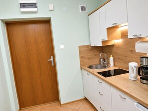 Eine kleine Küche mit Holztür, weißen Schränken, einem Spülbecken und einer Kaffeemaschine.