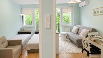 A modern apartment with a bed, sofa, dining table, and a view of greenery.