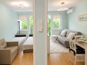 Ein modernes Apartment mit Bett, Sofa, Esstisch und Blick auf Grünflächen.