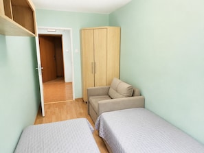 Eine kleine Einzimmerwohnung mit Holzschrank, einer Couch und zwei Einzelbetten.