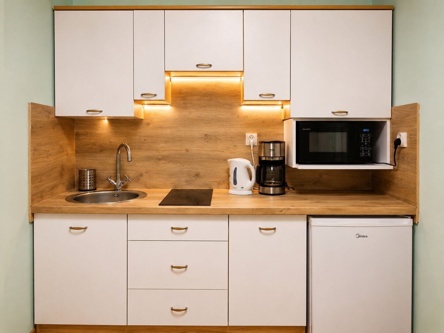 A compact kitchen with a sink, a coffee maker, a microwave, and wooden cabinets.