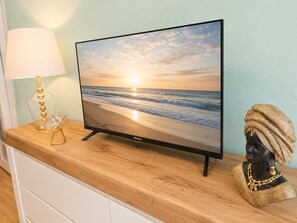 Ein Flachbildfernseher auf einer Holztischplatte, mit einer Strandansicht, einer Lampe und einer dekorativen Büste.