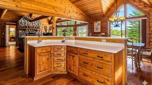 A spacious kitchen with wooden cabinets, a large island, and a stone fireplace. - Luxury log cabin on Spider Lake in Manitowish Waters (Manitowish Waters)