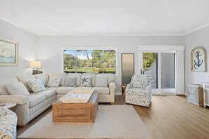 Ein Wohnzimmer mit Sofa, Sessel, Couchtisch und Blick ins Freie.