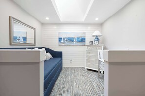 Ein Zimmer mit einem blauen Sofa, einem weißen Schminktisch, einem gerahmten Bild von Segelbooten und einem gemusterten Teppich.