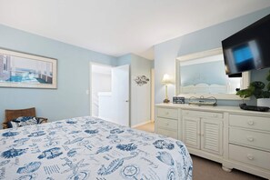 Ein Schlafzimmer mit einem Bett, einem Schminktisch, einem Fernseher und einem gerahmten Bild an der Wand.