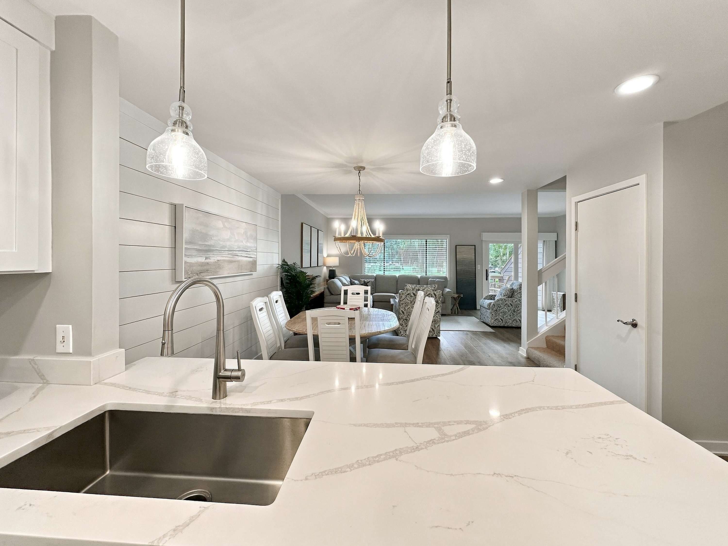A modern kitchen with a marble countertop, stainless steel sink, and pendant lighting.