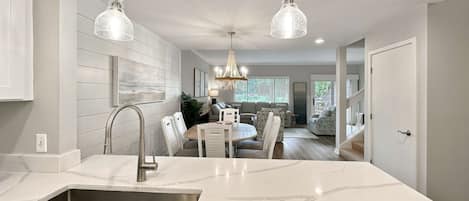 A modern kitchen with a marble countertop, stainless steel sink, and pendant lighting.