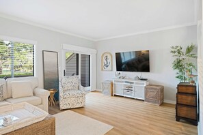 Ein Wohnzimmer mit Sofa, Sesseln, Fernseher und Holzboden.