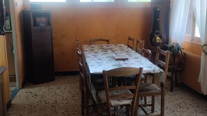 Un comedor con una mesa grande, sillas, ventilador de techo y ventanas.