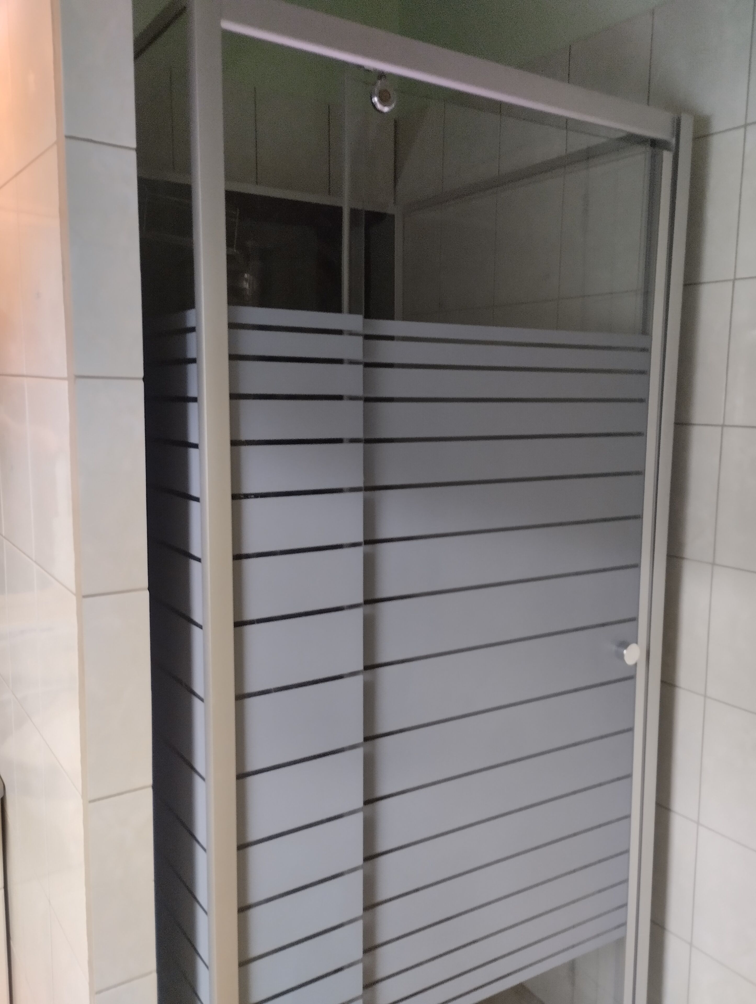 Une pièce dotée d’une porte-fenêtre coulissante, de murs recouverts de carreaux blancs et d’un espace douche visible.