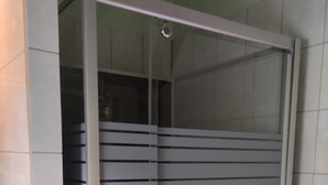 Una habitación con puerta de vidrio corredera, paredes de azulejos blancos y zona de ducha visible.