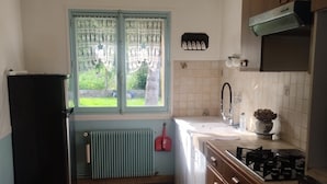 Una cocina con ventana, radiador, fregadero, estufa y armarios.