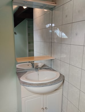 Ein Badezimmer mit einem weißen Waschbecken, einem Spiegel und einer raumhohen Fliesenwand.