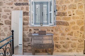Eine Steinsäule, ein Fenster mit Fensterläden, ein kleiner Tisch mit einem Korb und ein schwarzes Metallgitter.