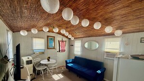 Une pièce avec un canapé bleu, une table à manger avec des chaises, un téléviseur et un appareil de climatisation.