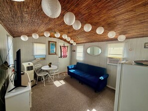 Ein Zimmer mit einem blauen Sofa, einem Esstisch mit Stühlen, einem Fernseher und einer Klimaanlage.
