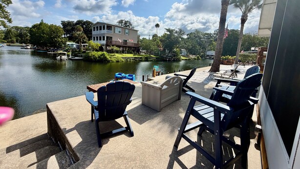 Une terrasse avec des chaises et une table, donnant sur un lac, avec des bâtiments et des arbres en arrière-plan.
