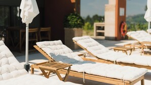 Une terrasse avec des chaises longues, une table et des parasols.