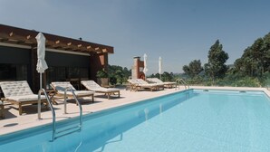 Un espace piscine avec des chaises longues et des parasols, un coin salon abrité et une vue sur les arbres et les collines.
