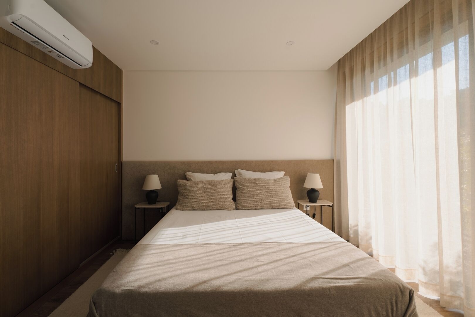 Ein Hotelzimmer mit einem Bett, zwei Nachttischen, Lampen, einer Klimaanlage und einem Fenster mit Vorhängen.