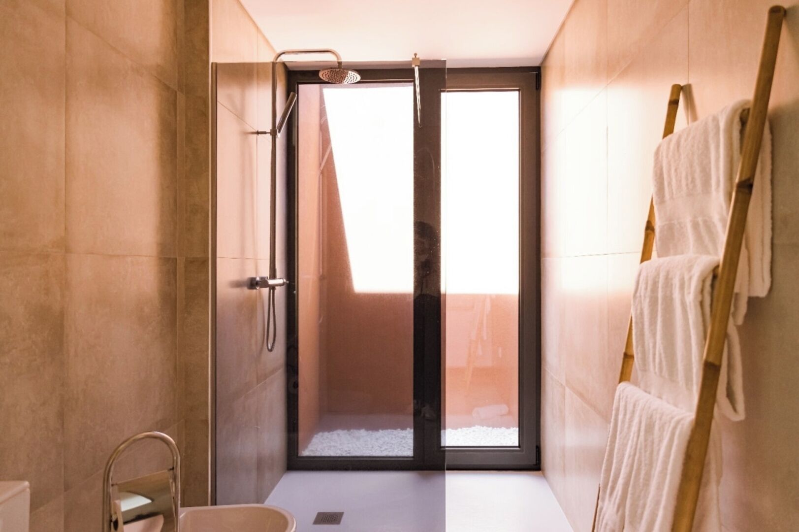 Ein modernes Badezimmer mit Duschkabine aus Glas, einem Handtuchhalter und einem sichtbaren Fenster.