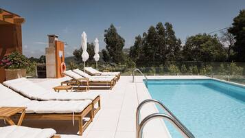 Ein Poolbereich mit Liegestühlen und Sonnenschirmen, ein klarer Himmel und Blick auf Bäume.