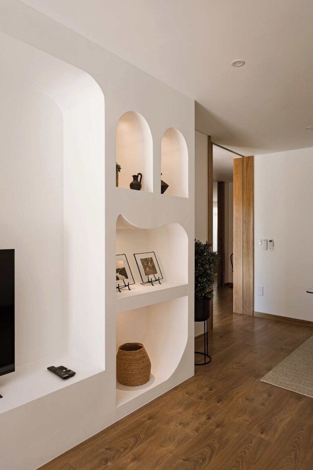 A modern interior with a curved white wall, wooden flooring, and a television on the left.