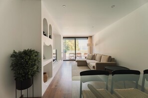 A modern living room with a sofa, a coffee table, and a TV. There is a plant and a glass table with chairs. - Souto Village 2 - by RowdHouses (Marco de Canaveses)