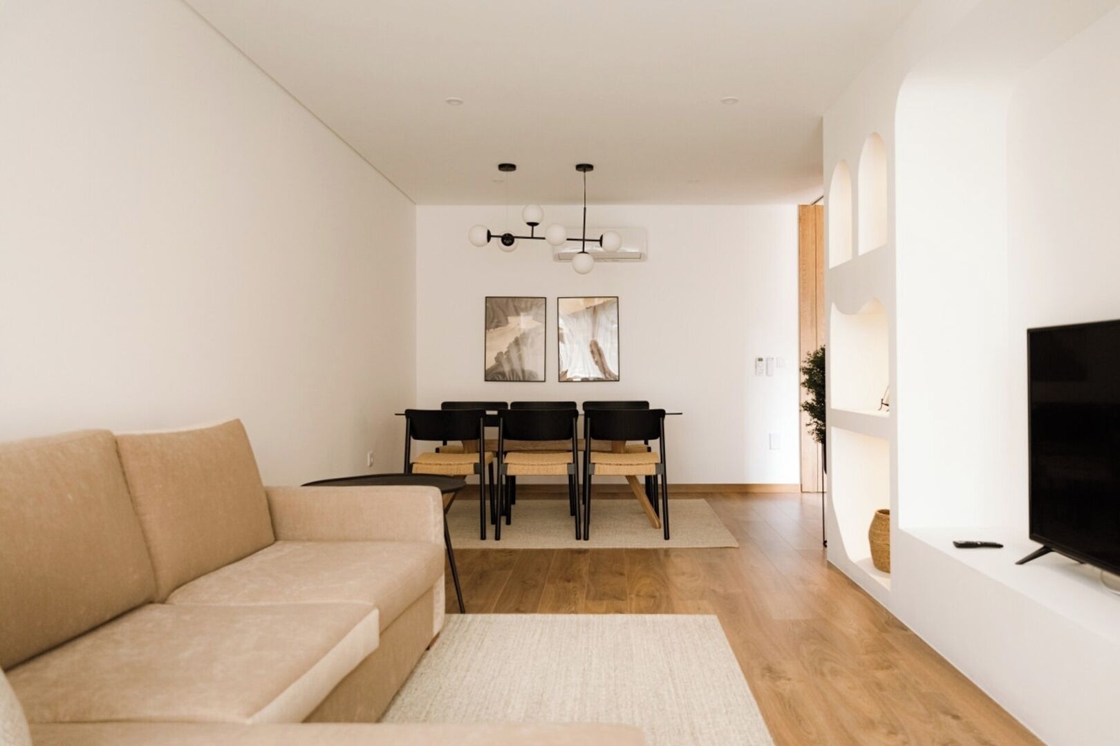 Ein modernes Wohnzimmer mit einer Couch, einem Esstisch, Stühlen, einem Fernseher und Kunstwerken an der Wand.